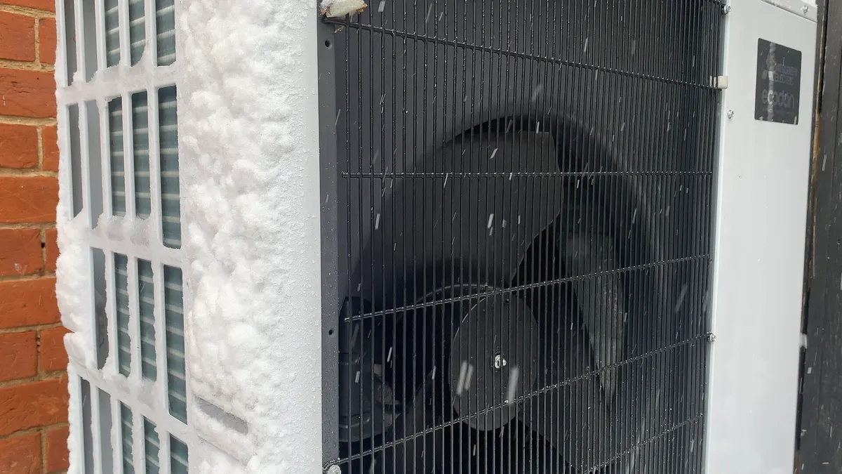 Unidad exterior de una bomba de calor aire-agua cubierta de nieve mientras funciona
